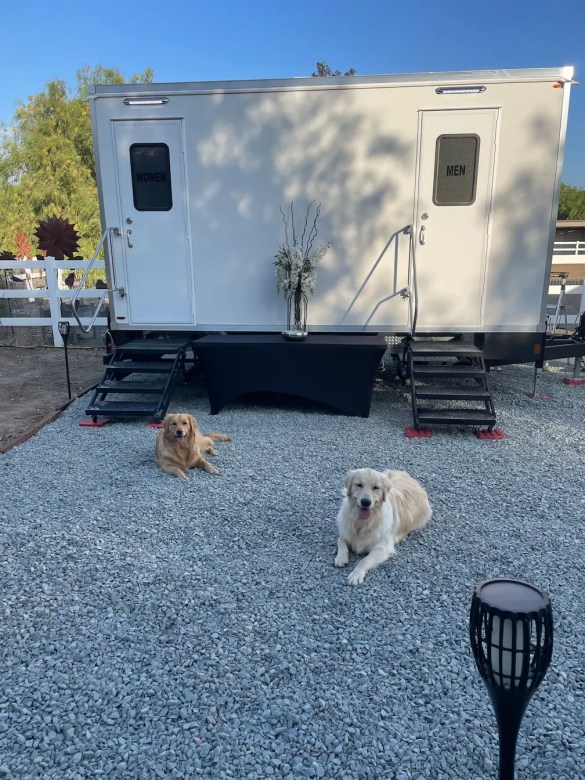 Luxury restroom trailer set up at a Temecula wedding with two dogs relaxing on the ground in front.