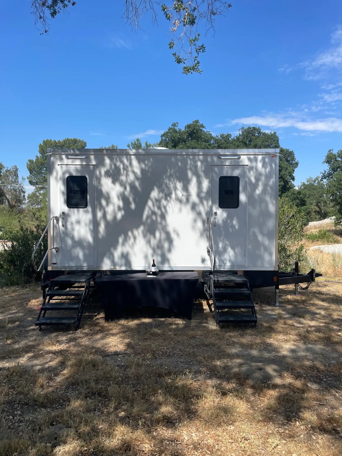 Luxury restroom trailer at an outdoor wedding in Hemet, CA with a table stationed in front.